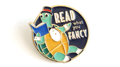 Enamel pin featuring a turtle who is all dressed up and reading a book