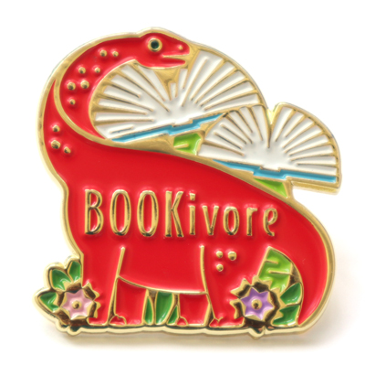 Enamel pin of a red sauropod eating a tree that resembles a book. Text on the dino's body says Bookivore