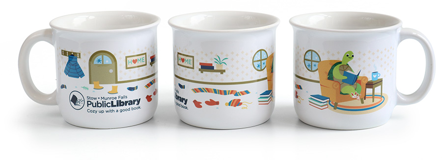 White campfire mug with library logo and a wrap-around image of Spike the turtle reading a book in a big orange armchair.